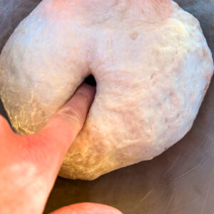 finger pressing into proofed pizza dough in bowl