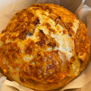 an artisan cheese bread loaf sitting on parchment paper in a Dutch oven.